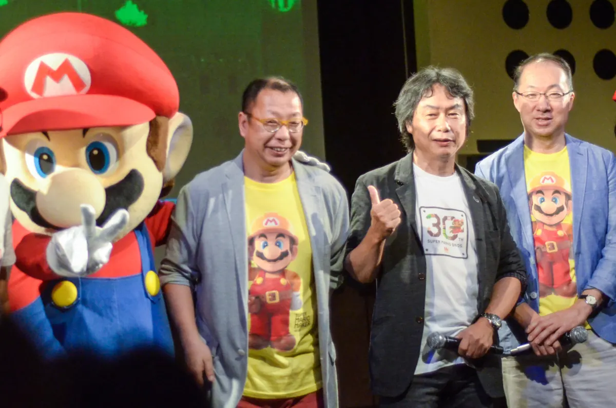 Drei Männer in bunten T-Shirts neben einer Mario-Figur